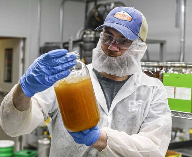 man in lab gown holding a bottle of hemp extract