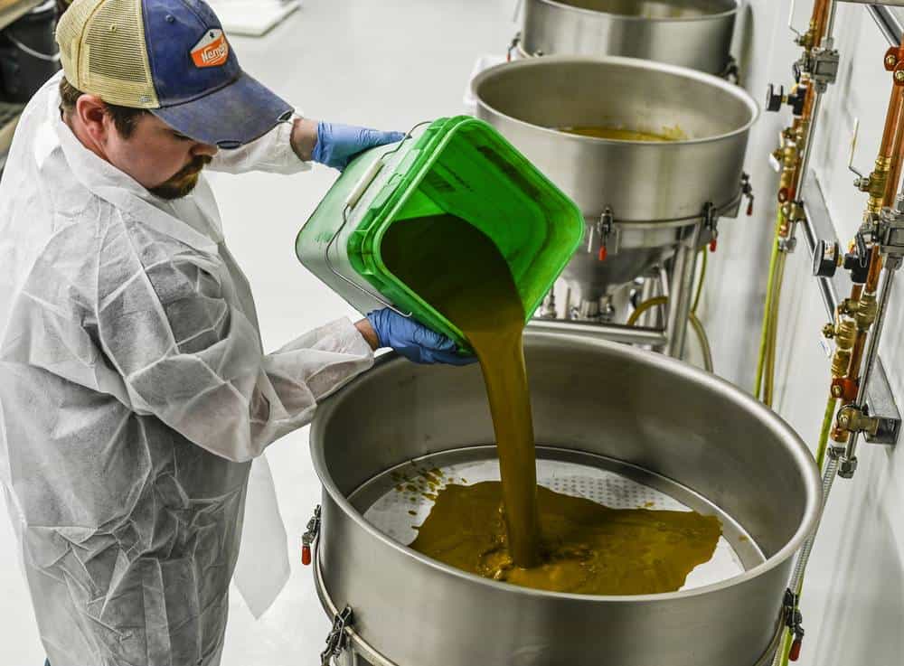 man in lab coat pouring extract in machine