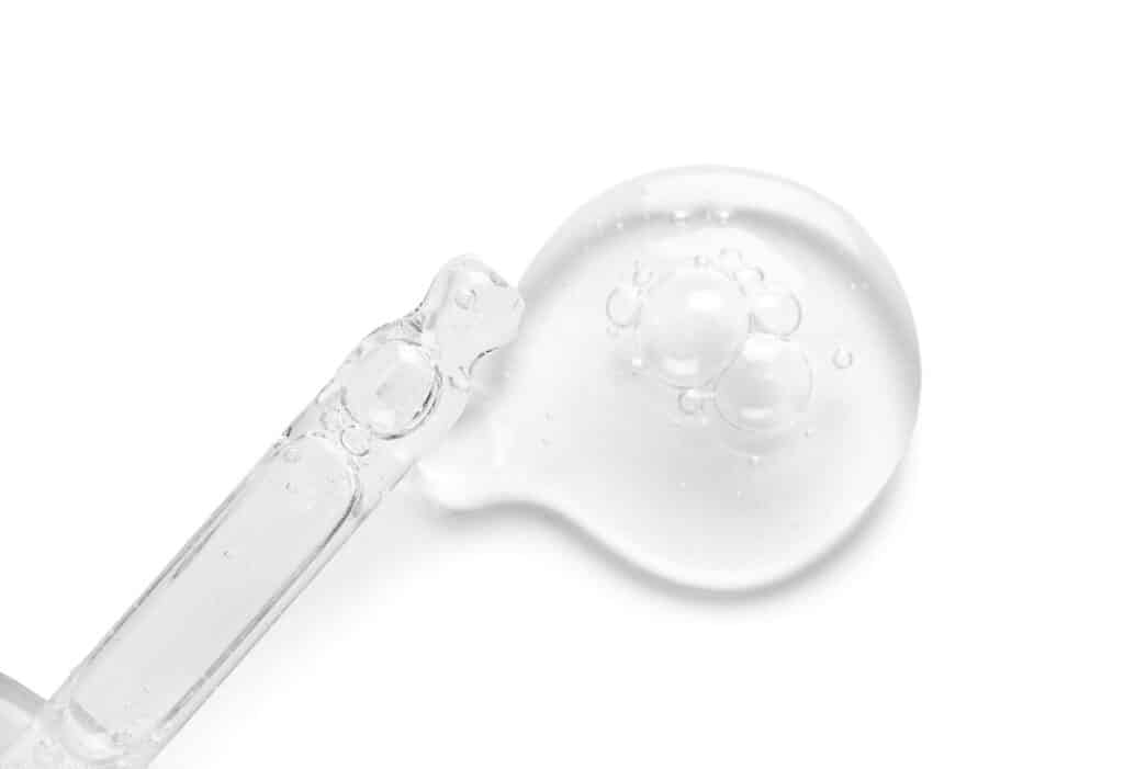 glass dropper and sample of cosmetic serum on white background